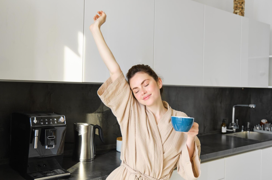 Woman stretching with coffee in a kitchen to illustrate the science behind morning routines